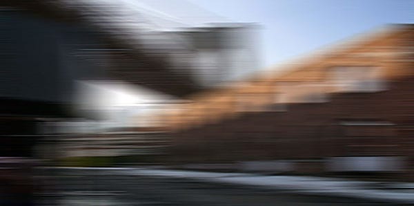 A blurred image of a building with a brick facade and a bridge-like structure in the foreground.