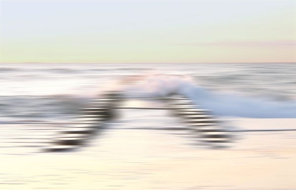 A blurred image of a beach with waves crashing against a wooden pier extending into the water.