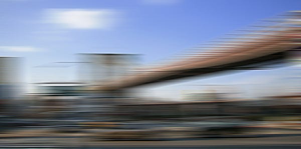 A blurred image of a cityscape with the Brooklinbridge and buildings under a blue sky.